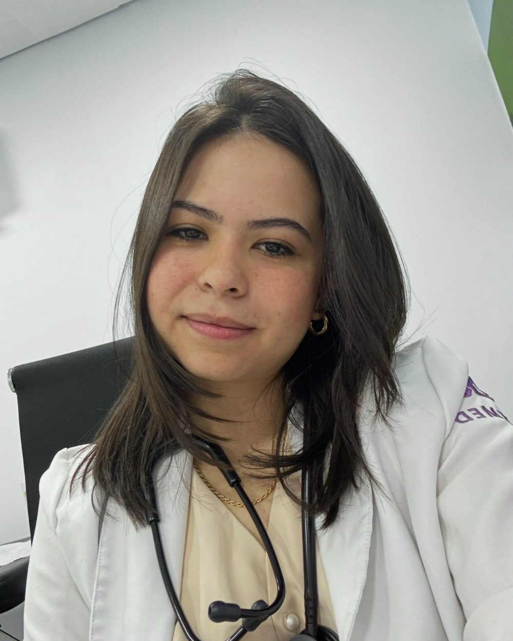 Dra. Taís Fernanda, de jaleco branco e estetoscópio, sentada no consultório.